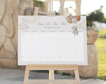 Könnte beinhalten: Ein weißer Kalender mit einem braunen Teddybär, der Ballons hält. Der Kalender steht auf einem Holzstaffelei und trägt die Aufschrift "Erraten Sie das Geburtsdatum von Baby Olivia".