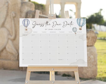 May include: A white calendar with blue and white hot air balloons printed on it. The calendar is on a wooden easel and says "Guess the Due Date of Baby Caleb".