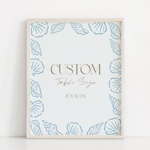 May include: A framed custom table sign with a light blue seashell border. The sign has the words "CUSTOM Table Sign" in gold lettering and the dimensions "8 X 10 IN". The frame is a light wood color.
