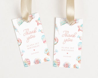 May include: Two white thank you tags with pink and blue watercolor illustrations of sweets and the text "Thank you, Alana is 1st Birthday, 12.01.20XX". The tags are attached to gold ribbon.