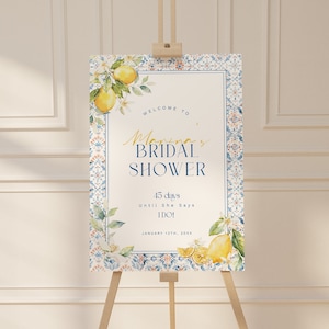 May include: A wooden easel displays a bridal shower sign. The sign features a lemon and floral design with the text "Welcome to Marina's Bridal Shower." It includes the date and countdown to the wedding. The sign has a decorative border.
