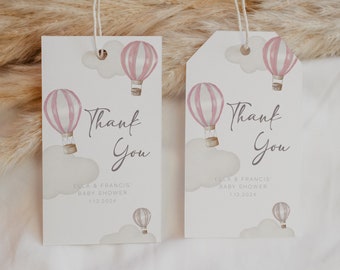 Può includere: Due etichette regalo per baby shower con un design ad acquerello. Ogni etichetta presenta una mongolfiera rosa, nuvole e le parole "Thank You". Le etichette includono anche il testo "Ella & Francis' Baby Shower" e la data.