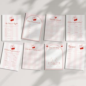 May include: A collection of baby shower game cards with a cherry theme. The cards feature pink and white striped backgrounds and red cherry illustrations. Games include "The Price is Right," "Baby Word Scramble," and "Draw the Baby."