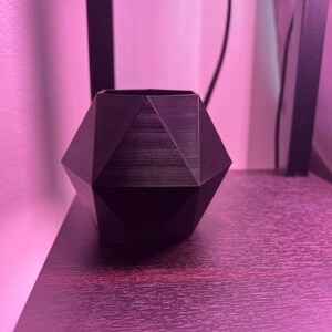 May include: A black geometric-shaped planter with a textured surface. The planter is sitting on a dark wood surface.