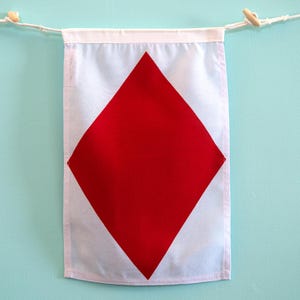 May include: A rectangular fabric wall banner featuring a large, solid red diamond shape centered on a light blue background. The banner has a white horizontal header at the top, suspended by a white cord with two small wooden toggles.