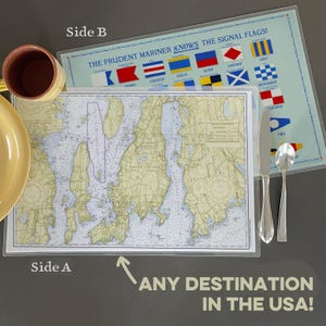 May include: A double-sided placemat featuring a nautical map of Rhode Island on one side and signal flags on the other. The text "THE PRUDENT MARINER KNOWS THE SIGNAL FLAGS!" is visible. The placemat is next to a yellow plate and a mug.