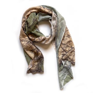 May include: A beige, green, and white scarf with a vintage map print. The map features lines, text, and a compass rose.
