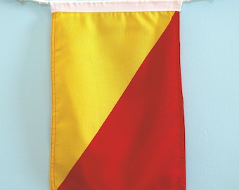 May include: A rectangular pennant flag divided diagonally into a yellow section on the left and a red section on the right. The top edge features a white fabric header with a white cord and two small wooden toggles for hanging the banner.