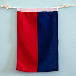 May include: A rectangular fabric wall banner featuring a vertical split design with a bright red left side and a deep navy blue right side. The banner is suspended from a white rope with wooden toggles and has a white fabric header at the top.