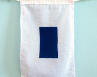 May include: A rectangular white fabric wall banner featuring a centred solid dark blue vertical rectangle. The banner is suspended from a white cord with small wooden toggles at each end, creating a clean and simple display for wall decor.