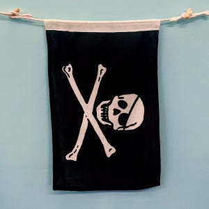 Puede incluir: Una bandera pirata negra con un diseño de calavera y huesos cruzados blancos. La calavera tiene un parche en el ojo.