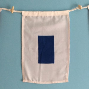May include: A white nautical signal flag with a blue square in the centre. The flag is hanging from a string with wooden clothes pegs.