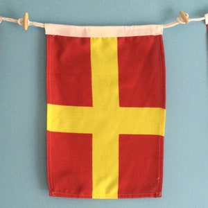 Pode incluir: Uma bandeira de sinalização náutica vermelha e amarela com uma borda branca e uma corda.