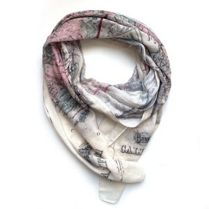 May include: A white scarf with a vintage map print in shades of pink, green, and blue. The map features the text "GALLIA" and "CO" in the bottom right corner.
