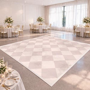 May include: A large, light-colored checkered dance floor dominates the center of a spacious room. The floor's pattern is a mix of light beige and off-white squares. Round tables with white tablecloths and floral centerpieces are set up around the room, ready for a special event.