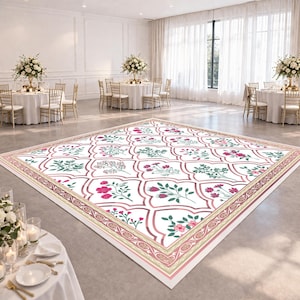 May include: A patterned dance floor in a wedding setting. The floor has a white base with a repeating floral design in pink and green, enclosed by a pink and gold border. Tables with white cloths and floral arrangements are visible in the background.