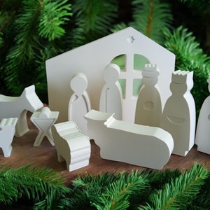 Könnte beinhalten: Eine weiße Krippe aus Holz mit Stall, Figuren der Heiligen Familie, den Heiligen Drei Königen und Tieren. Die minimalistischen Figuren sind ideal für Weihnachtsdekorationen.