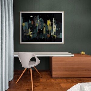 May include: An abstract cityscape art print in a wooden frame hangs above a modern desk. The artwork features buildings in shades of teal, yellow, and black against a dark background. A gray chair with wooden legs sits in front of the desk.