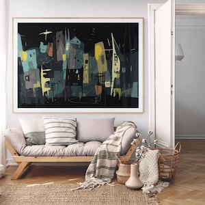 May include: Abstract art print featuring a cityscape in shades of teal, yellow, and gray against a black background. The artwork is framed in a natural wood frame and hangs above a wooden sofa with pillows and a blanket. The room has a neutral color palette.