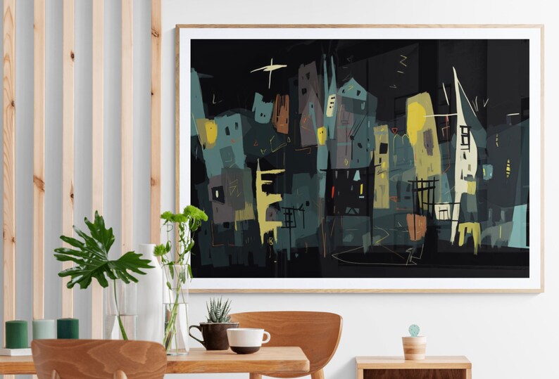 May include: Abstract cityscape art print in a wooden frame. The artwork features a dark background with stylized buildings in shades of teal, yellow, and brown. A star-like shape is visible in the upper left corner. The print is displayed on a wall above a wooden table.
