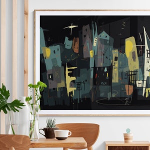 May include: Abstract cityscape art print in a wooden frame. The artwork features a dark background with buildings in shades of teal, yellow, and brown. A star-like shape is visible in the upper left corner. The print is displayed on a wall above a wooden table.