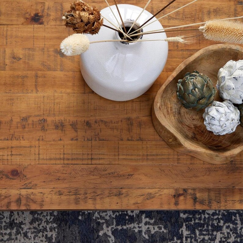 May include: A wooden table top with a white ceramic vase filled with dried flowers and a wooden bowl with three decorative artichokes. The table top has a rustic, distressed look.