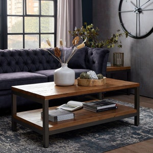 May include: A rustic wooden coffee table with a metal frame and a lower shelf. The table has a distressed wood finish and is decorated with a vase of dried flowers, a bowl of decorative items, and a stack of books.