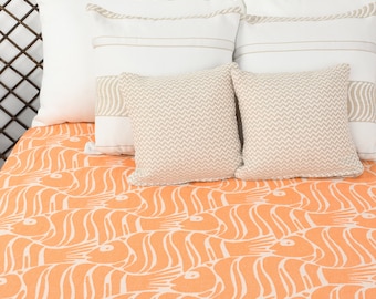 Puede incluir: Una cama con una cabecera blanca y un edredón naranja y blanco estampado. La cama está hecha con almohadas blancas y varios cojines de decoración beige y blanco.