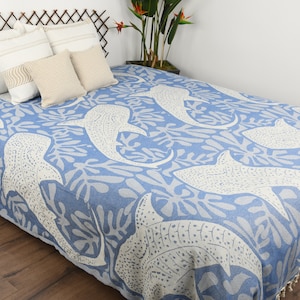 May include: A blue and white throw blanket with a pattern of whale sharks and seaweed. The blanket is on a bed with white pillows.