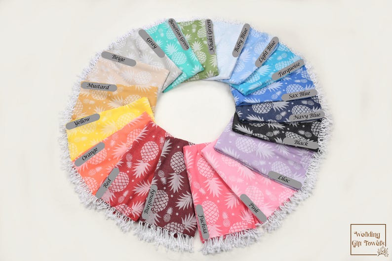 May include: A selection of beach towels in various colours, each featuring a pineapple pattern. The towels are arranged in a circle, with the colours ranging from yellow to blue.