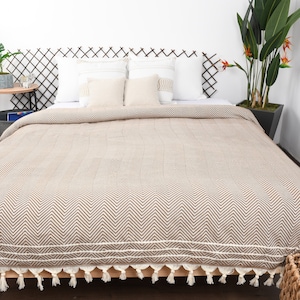 May include: A brown and white chevron patterned throw blanket with white tassels on a bed with white pillows.
