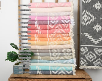 May include: A stack of Turkish towels in various colors, including pink, red, orange, beige, green, blue, and black. The towels have a white geometric pattern and are displayed on a wooden shelf. The text "wedding Gin Towels" is visible in the top left corner of the image.
