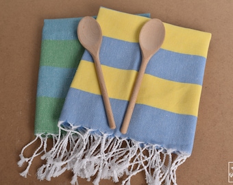Puede incluir: Dos toallas de cocina a rayas con flecos blancos, dobladas y presentadas con dos cucharas de madera.