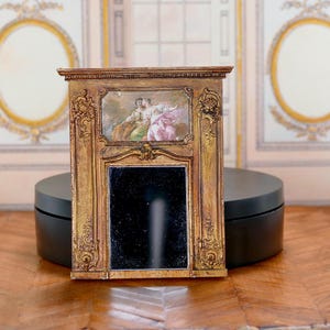 May include: A miniature gold-painted wooden fireplace mantel with a black mirror and a painted scene of two people in a landscape.