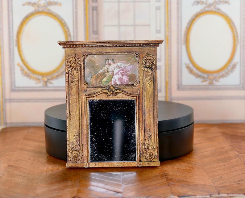 May include: A miniature gold-painted wooden fireplace mantel with a black mirror and a painted scene of two people in a landscape.