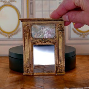 May include: A miniature gold-framed mirror with a decorative design and a small painting of two figures in the top section.