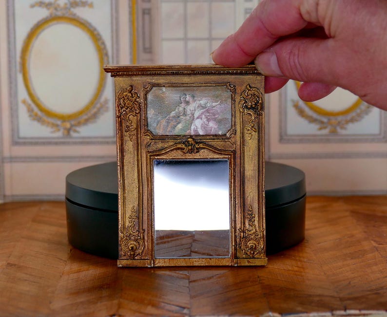 May include: A miniature gold-framed mirror with a decorative design and a small painting of two figures in the top section.
