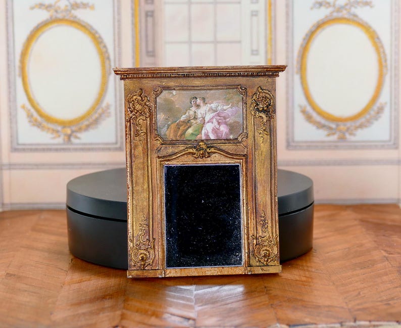 May include: A gold-framed antique mirror with ornate carvings and a black mirror surface. The mirror has a small painting of two figures in a landscape scene.