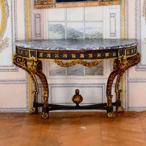 Può includere: Un tavolo console ornato in nero e oro con un piano in marmo. Il tavolo presenta sculture intricate e una base decorativa.