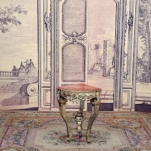 May include: Miniature antique table with a red marble top and ornate gold-colored legs. The table has a decorative, curved design and is set on a floral patterned rug. The background features a detailed illustration of a door and landscape.
