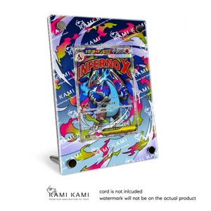 Puede incluir: Un marco de exhibición acrílico transparente con un diseño colorido, que contiene una carta de Pokémon con un dragón azul y rojo. El marco tiene un soporte y el texto "KAMI KAMI" e "INFERNOX" es visible.