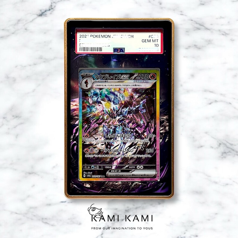 May include: A framed Pok&eacute;mon trading card featuring a colorful illustration of a creature with Japanese text. The card is graded as GEM MT 10 by PSA and is encased in a gold-colored frame. The frame has the text "2021 POKEMON" on the top.