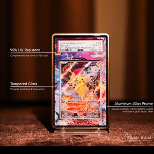 May include: A framed Pok&eacute;mon trading card featuring Pikachu. The card is encased in a gold-colored aluminum alloy frame with tempered glass and 95% UV resistance. The frame is displayed on a clear stand.