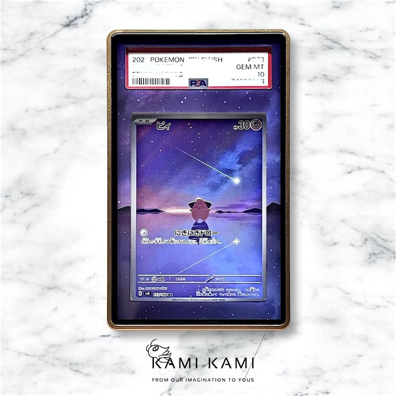 May include: A graded Pok&eacute;mon card in a gold-colored case. The card features a cartoon character against a purple and blue starry sky background. The case has text that reads "202 POKEMON" and "GEM MT 10". The bottom of the case has the text "KAMI KAMI".
