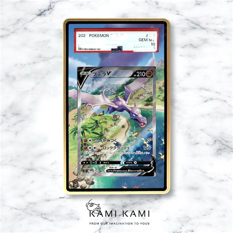 Op de afbeelding: Een ingelijste Pok&eacute;mon-kaart met een paarse Aerodactyl V-kaart met Japanse tekst. De kaart is beoordeeld en ingekapseld in een goudkleurig frame. De illustratie van de kaart toont een vliegend wezen boven een tropisch eiland.