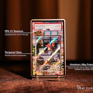 May include: A framed Pok&eacute;mon card featuring a Charmander illustration. The card is encased in a gold-colored aluminum alloy frame with tempered glass. The frame is designed to protect the card from scratches and UV light. The frame is displayed on a clear stand.