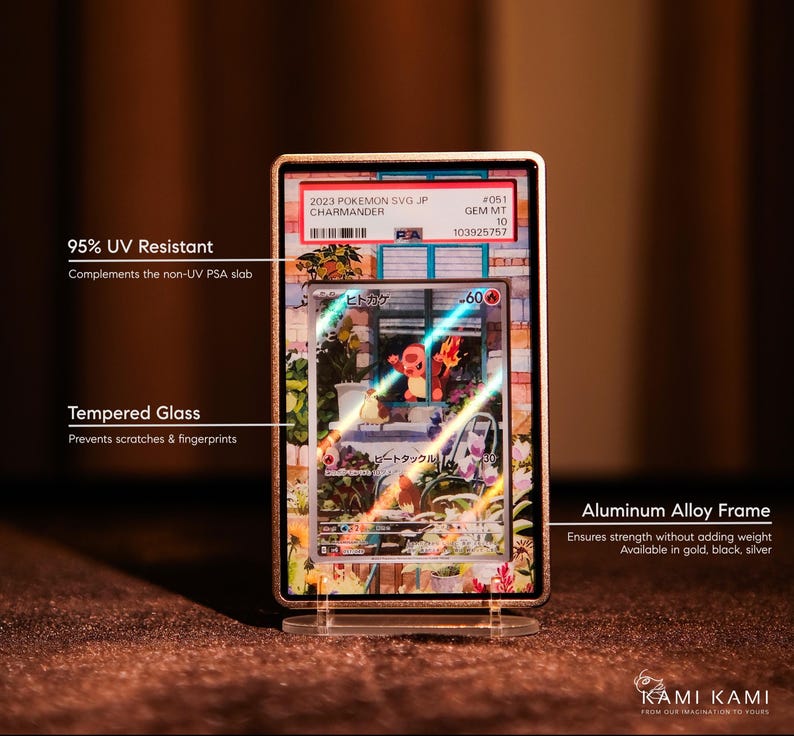 May include: A framed Pok&eacute;mon card featuring a Charmander illustration. The card is encased in a gold-colored aluminum alloy frame with tempered glass. The frame is designed to protect the card from scratches and UV light. The frame is displayed on a clear stand.
