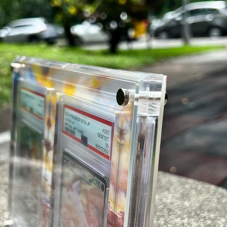 May include: Clear acrylic display case with a graded trading card inside. The card is labeled with text including "Pokemon SV7a JP" and "GEM MT 10". The case is held together with small, silver-colored screws.