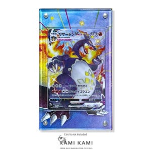 Puede incluir: Una vitrina de acr&iacute;lico transparente con un fondo morado y azul. La vitrina contiene una carta de comercio de Pokemon japonesa con una imagen hologr&aacute;fica de Charizard VMAX. El texto de la carta dice "リザードン VMAX 330".