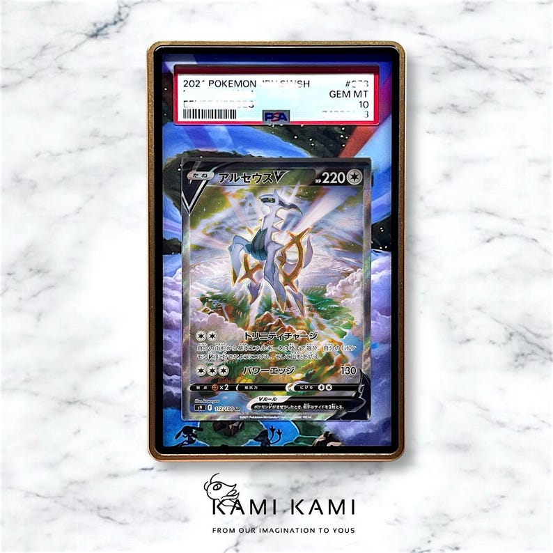Puede incluir: Una carta coleccionable de Pok&eacute;mon calificada con el personaje Arceus V, con texto en japon&eacute;s. La carta est&aacute; dentro de un soporte protector con un marco dorado. El soporte tiene una calificaci&oacute;n PEA de GEM MT 10.